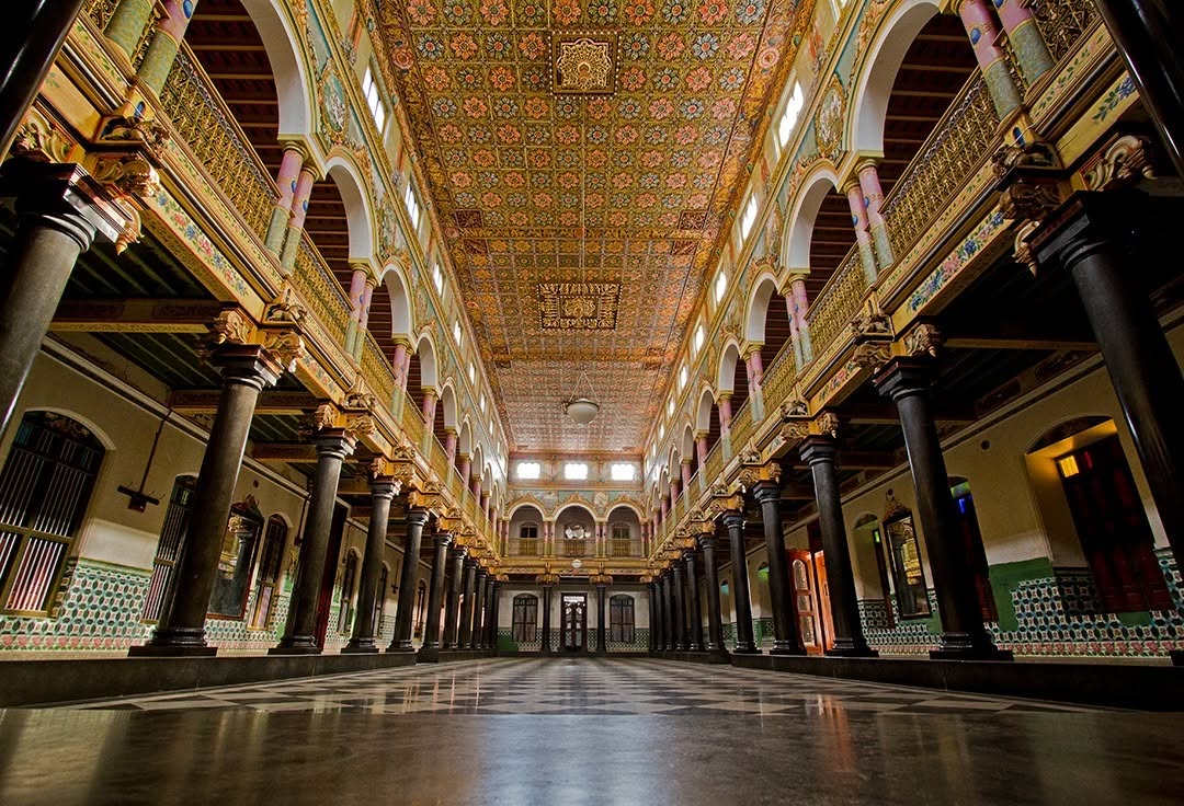 Grand interior courtyard of Athangudi Palace in Chettinad featuring traditional pillars, carved ceilingss and handmade Athangudi tiles